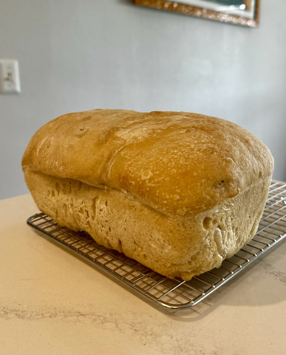 A tall sourdough sandwich loaf cooling on a wire rack